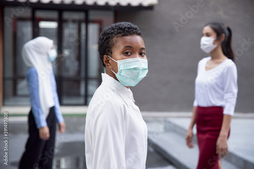 Black African woman wearing face mask, observing new normal lifestyle of social distancing, keeping distance away from other people in public
