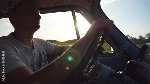 Wallpaper Mural Caucasian man holding hands on steering wheel and driving a retro car at sunset. Profile of guy traveling in a vintage vehicle at countryside. Low angle view Slow motion Close up Torontodigital.ca
