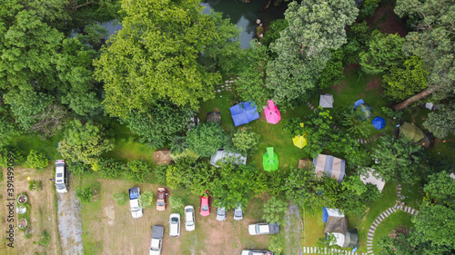 Aerial view of colorful tents in the garden with green plants, and car.