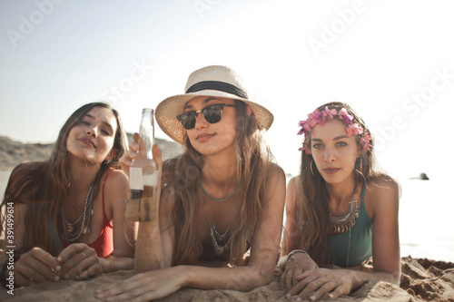 three beautiful girls lying on the beach drink a beer from a bottle