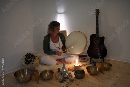 Woman sitting with a drum in her hands for a sound healing session with many sound healing instruments in front of her with singing bowls, koshi chimes, drum, sansula & zimbel photo