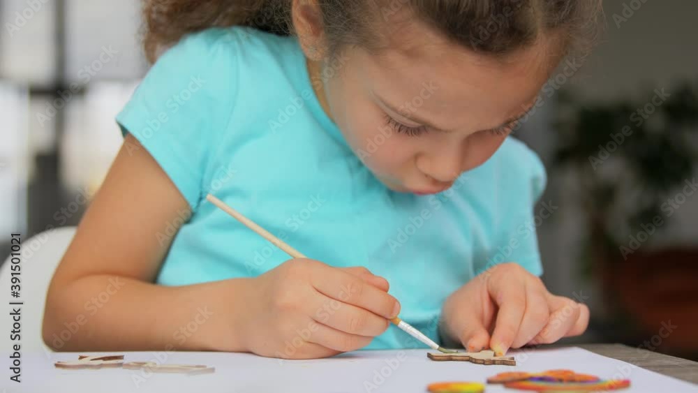 childhood, hobby and leisure concept - little girl with brush coloring wooden craftwork items at home childhood, hobby and leisure concept - little girl with brush coloring wooden craftwork items at home