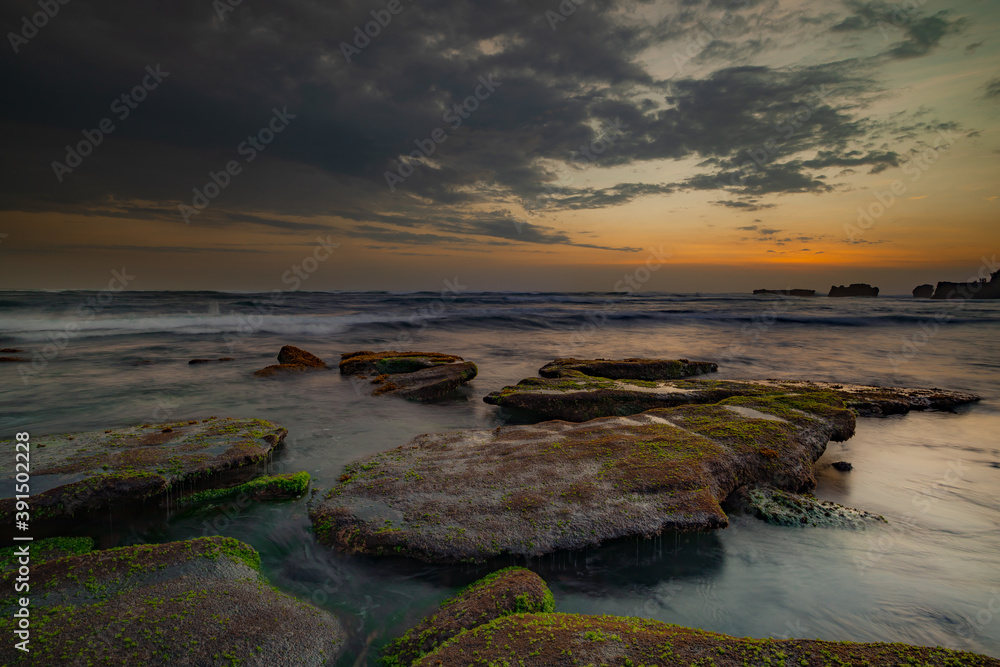 Calm ocean long exposure. Stones in mysterious mist of the sea waves. Concept of nature background. Sunset scenery background. Mengening beach, Bali, Indonesia.