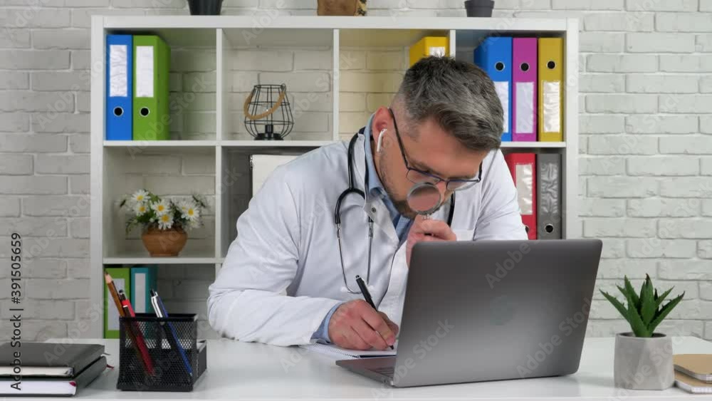 Doctor wear white coat wireless earphones in hospital office writes diagnosis in notebook looks magnifying glass. Medical worker examines patient client online remote video call laptop computer webcam Doctor wear white coat wireless earphones in hospital office writes diagnosis in notebook looks magnifying glass. Medical worker examines patient client online remote video call laptop computer webcam