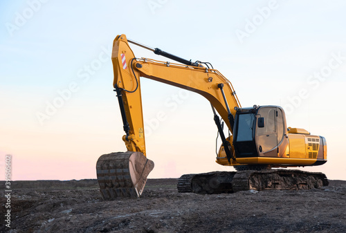 Excavator working on earthmoving at open pit mining. Backhoe digs sand and gravel on sunset background. Heavy construction equipment for quarrying. Excavation at construction site.