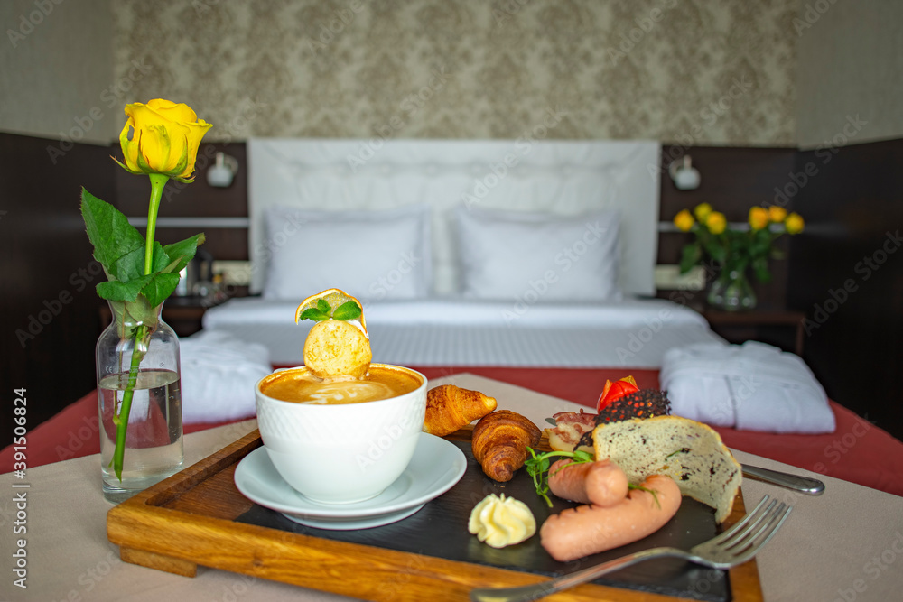 Breakfast in the hotel room. Morning coffee in a white cup with croissants, sausages and bread on a tray on the background of a double bed in a hotel room.
Breakfast in the hotel room. Morning coffee in a white cup with croissants, sausages and bread on a tray on the background of a double bed in a hotel room.