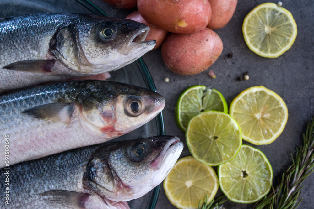 Fresh ingredients top view photo. Trout fish with potatoes, lemon slices and rosemary on gray table. Fresh ingredients top view photo. Trout fish with potatoes, lemon slices and rosemary on gray table.