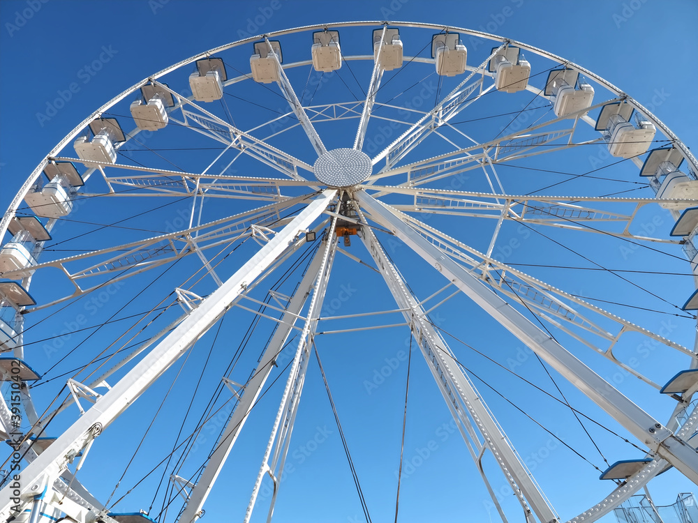 White ferris wheel with empty gondolas and blue sky