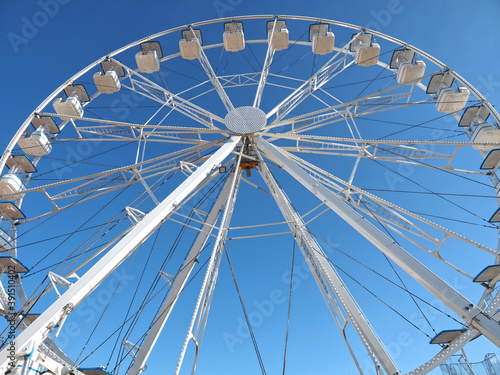 White ferris wheel with empty gondolas and blue sky