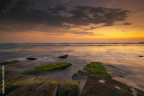 Calm ocean long exposure. Stones covered by green moss in mysterious mist of the sea waves. Concept of nature background. Sunset scenery background. Mengening beach  Bali  Indonesia.