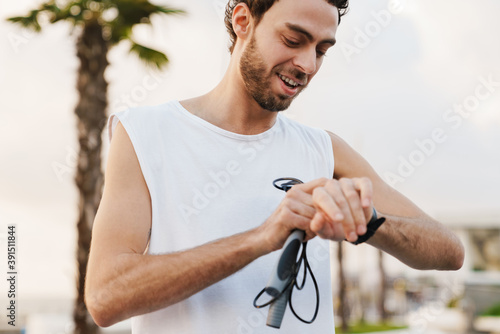 Pleased guy looking at wristwatch while working out with jump rope