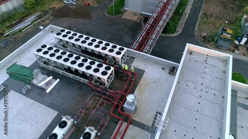 Engineers or workers in overalls and helmets check an industrial ventilation and air conditioning system on the roof of a building. Top-down aerial view