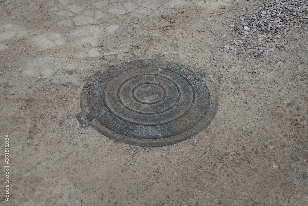 one black iron manhole lying on gray sand and concrete outside
