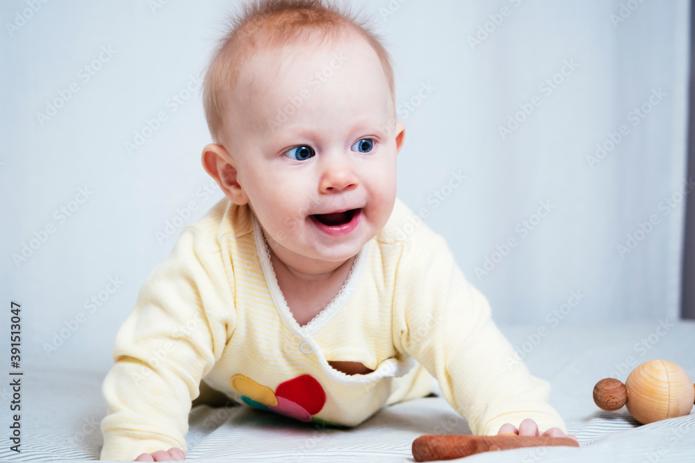 A seven-month-old girl is happy, smiling and playing with wooden toys, lying on her stomach in a bright room A seven-month-old girl is happy, smiling and playing with wooden toys, lying on her stomach in a bright room