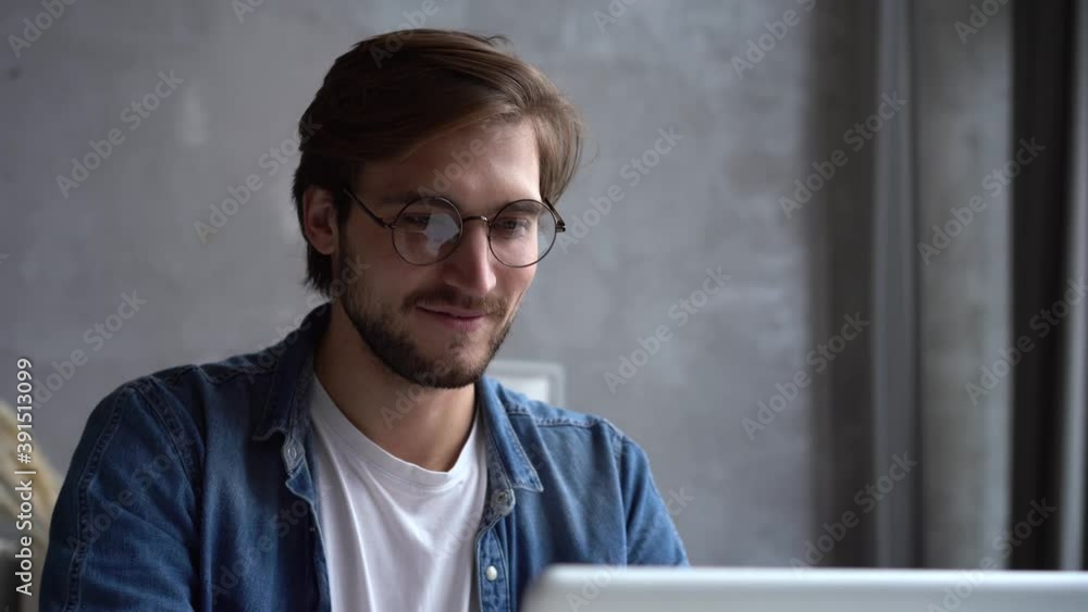 Smiling businessman working on laptop computer at home office. Male professional typing on laptop keyboard at workplace. Portrait of positive business man looking at laptop screen indoors