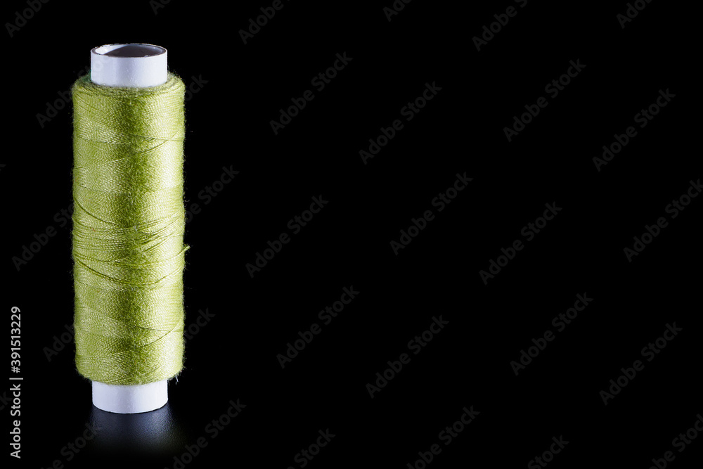 Reel with green sewing silk threads isolated on a black background, close-up, copy space. Bright background for sewing and needlework Reel with green sewing silk threads isolated on a black background, close-up, copy space. Bright background for sewing and needlework