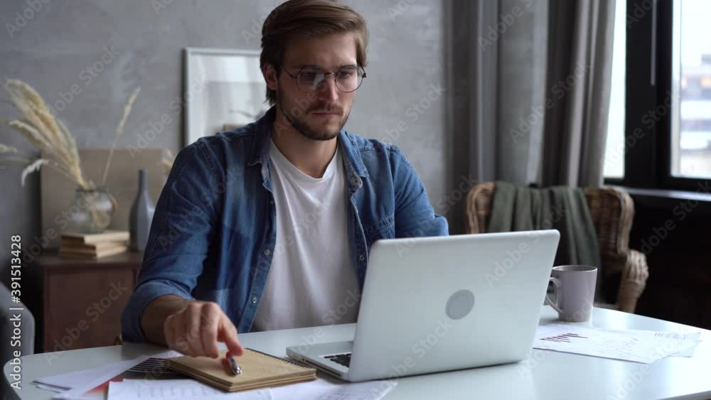 Smiling businessman working on laptop computer at home office. Male professional typing on laptop keyboard at workplace. Portrait of positive business man looking at laptop screen indoors