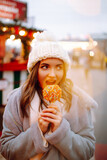Happy woman on Christmas market with caramelized apple. Outdoor activities on Christmas and New Year. Young woman enjoying winter moments. Lights around.