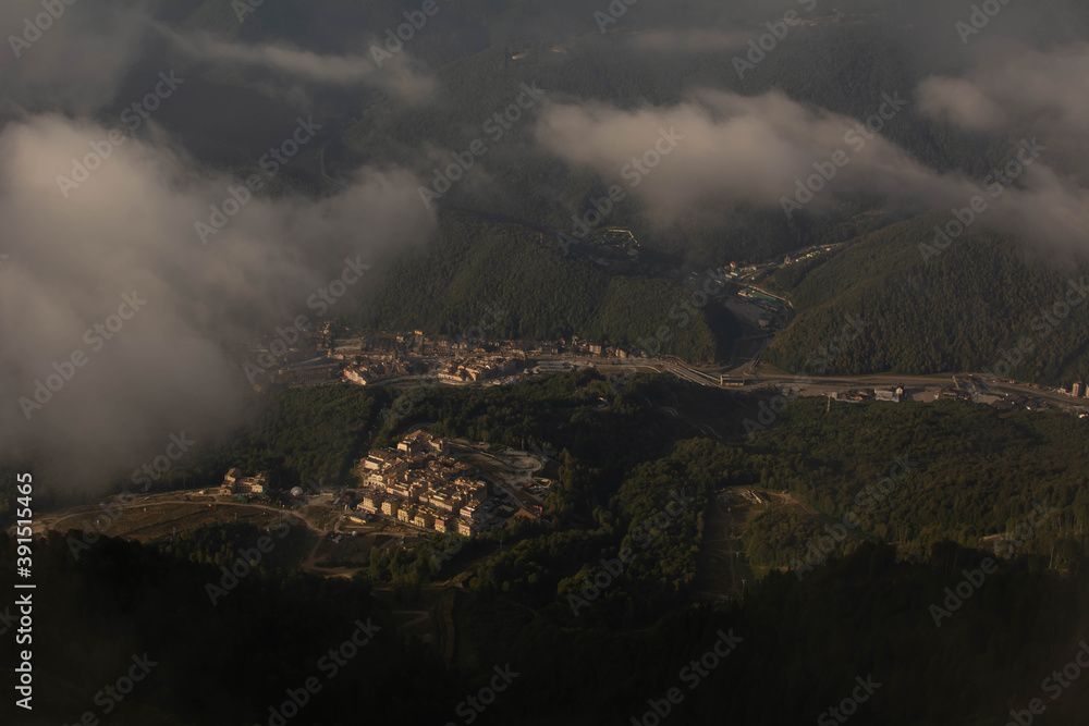 Fototapeta premium view from the top of the mountain through the clouds to the valley in the sunlight