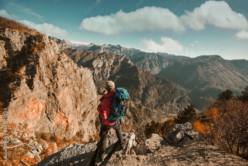 Hiker man with backpack standing on edge of cliff and looking at the mountains