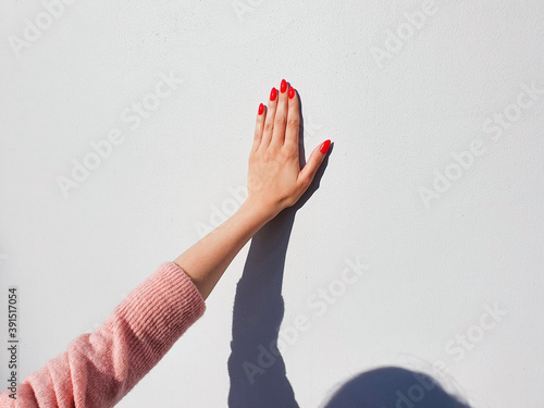 Φωτογραφία Female hand with red nails and shadow on gray wall, high five sign