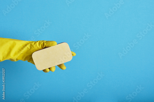 Hand in yellow glove with sponge on blue background