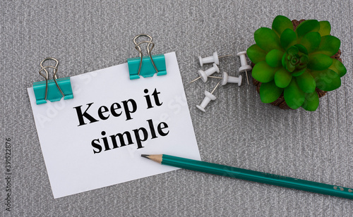 KEEP IT SIMPLE - words on a white sheet with clips on a gray background with cactus, pencil photo