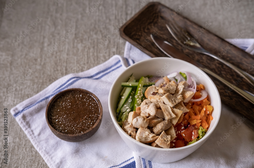 Fototapeta premium Healthy organic chicken Hawaiian poke bowl with cucumber, rice, carrots, onion served in bowl on table decorated with kitchen napkin. Healthy lifestyle