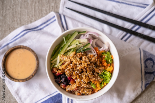 Healthy organic vegetarian poke bowl with tofu, fermented soybeans- tempeh, cucumber, rice, carrots, onion served in bowl on table decorated with kitchen napkin. Healthy lifestyle photo