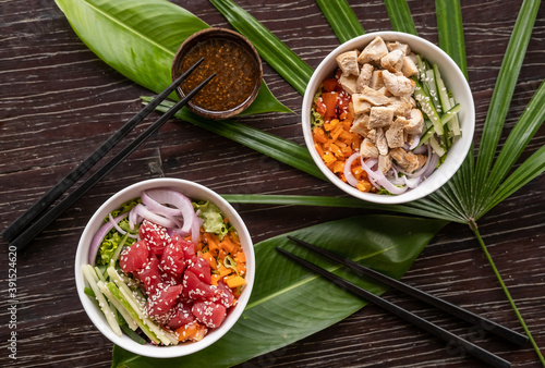 Variety of healthy organic poke bowls with tuna, chicken, tofu and cucumber, rice, carrots, onion served on wooden table with tropical leaves. Healthy lifestyle