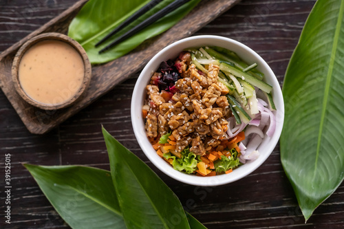 Healthy organic vegetarian poke bowl with tofu, fermented soybeans -tempeh, cucumber, rice, carrots, onion served in bowl on wooden table with tropical leaves. Healthy lifestyle
