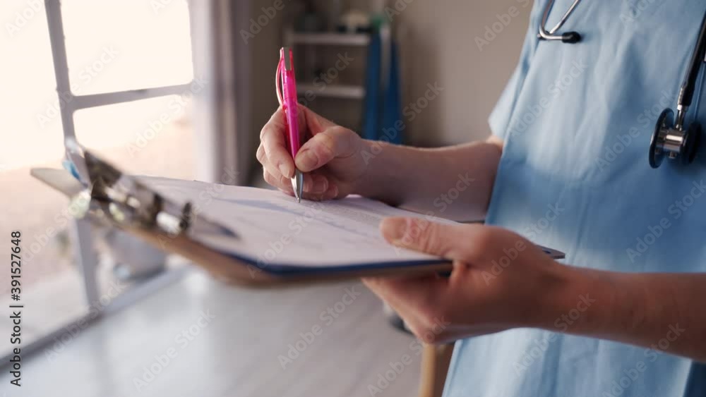 Close-up of a female physiotherapist writing a medical report on clipboard with pen in clinic Close-up of a female physiotherapist writing a medical report on clipboard with pen in clinic
