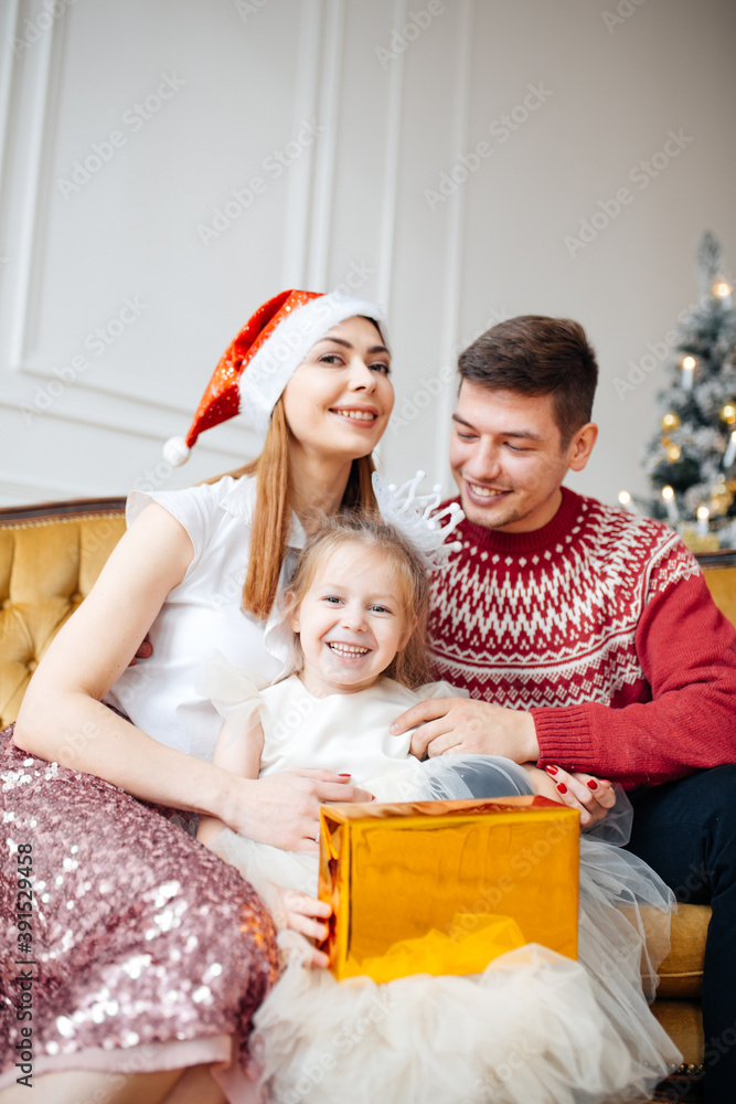 A child girl in an elegant dress sits on the lap of her parents with a gift in her hands. Concept for christmas, new year gifts A child girl in an elegant dress sits on the lap of her parents with a gift in her hands. Concept for christmas, new year gifts