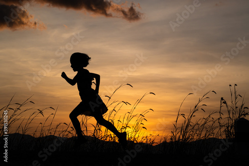 Silhouette of child girl running on the meadow at sunset background.