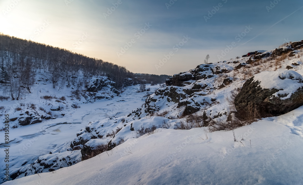 Winter landscape with frozen river, snow, rocks and trees