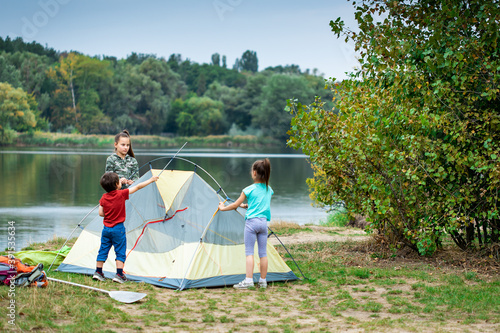 Three children pitching tent together near lake © Olena Shvets