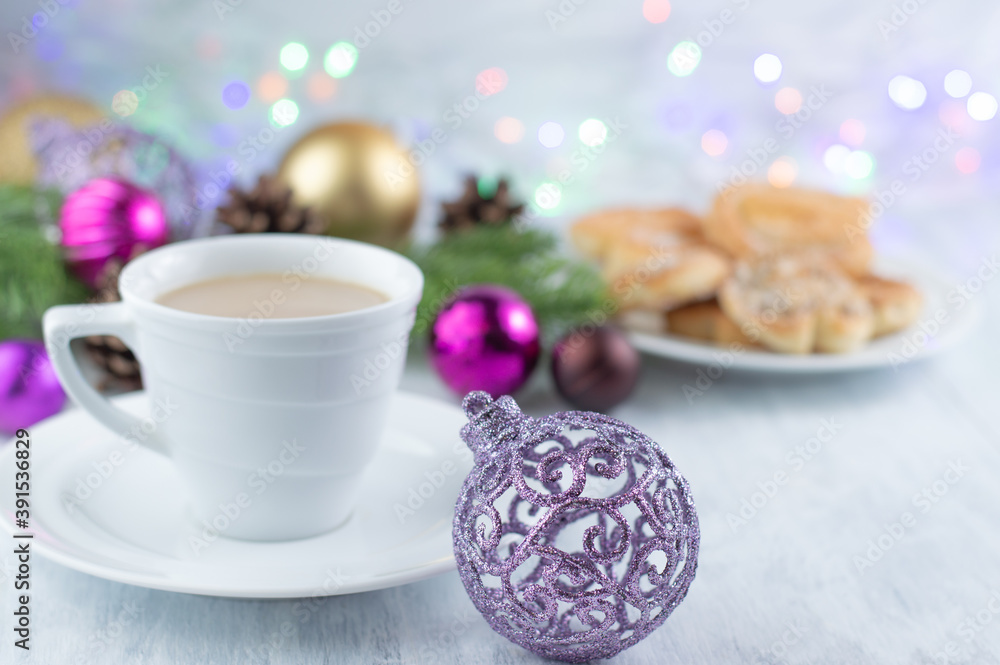 Christmas background with a purple ball on the foreground and a blurred image of a cup of coffee with milk, cookies, sprigs of fir and Christmas balls. Christmas background with a purple ball on the foreground and a blurred image of a cup of coffee with milk, cookies, sprigs of fir and Christmas balls.