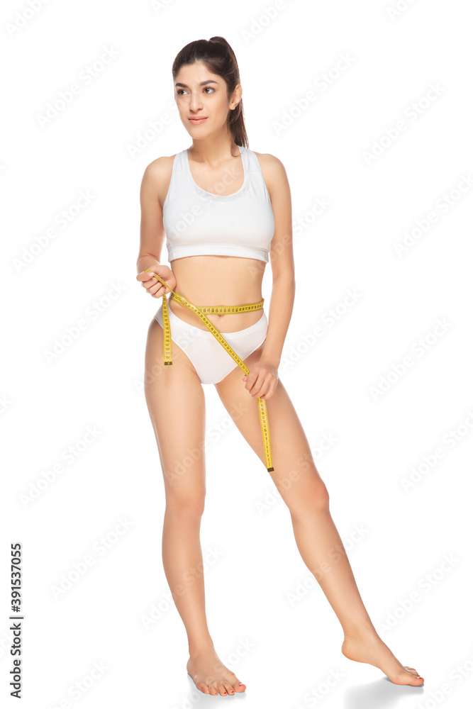 Fototapeta premium Tape measure. Beautiful female model on white background. Beauty, cosmetics, spa, depilation, diet and treatment, fitness concept. Fit and sportive, sensual body with well-kept skin in underwear.