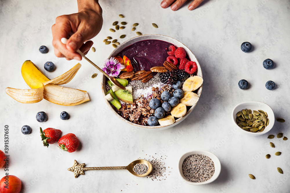 A woman is eating an açai bowl with fresh fruits for breakfast with banana, blueberries, blackberries, strawberries, kiwi, nuts and seeds. A woman is eating an açai bowl with fresh fruits for breakfast with banana, blueberries, blackberries, strawberries, kiwi, nuts and seeds.