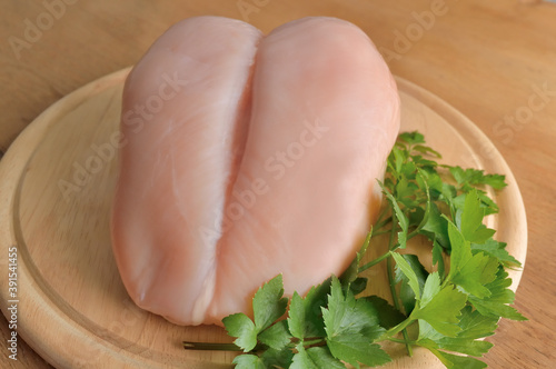 uncooked raw chicken breast with parsley leaves on a wooden cutting board, ingredient for preparing delicious meal
