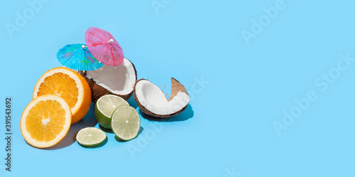 Fresh juicy orange, coconut and green lime with a cocktail umbrella isolated on blue background. Concept of Healthy eating and dieting. Travel and holiday concept. Copy space. Free space for your text