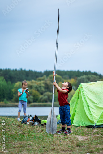 Little preschool boy playing with paddle near tent on the river bank in camping site