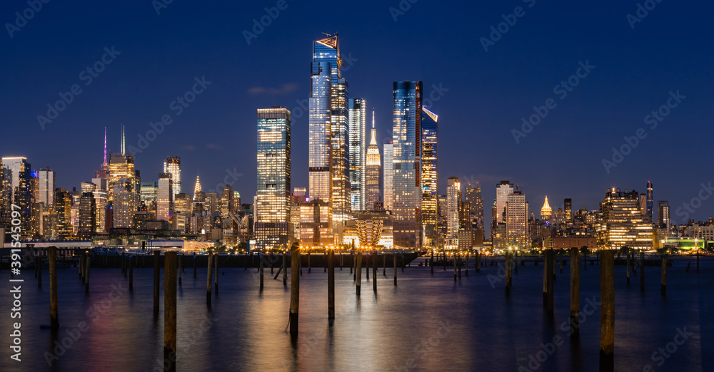 New York City evening panoramic of Manhattan Midtown West skyline with illuminated Hudson Yards skyscrapers from the Hudson River. NYC, USA New York City evening panoramic of Manhattan Midtown West skyline with illuminated Hudson Yards skyscrapers from the Hudson River. NYC, USA