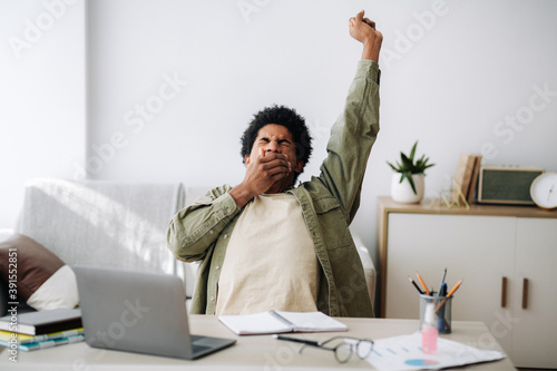 Tired black student yawning and stretching during his remote studies from home photo