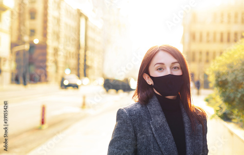 Redhead caucasian woman on a bright sunny empty street in black protective mask. Revival after coronavirus.