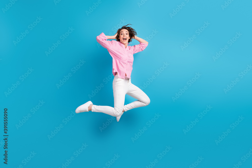 Full size photo of crazy impressed girl jump touch hands head isolated over blue pastel color background Full size photo of crazy impressed girl jump touch hands head isolated over blue pastel color background