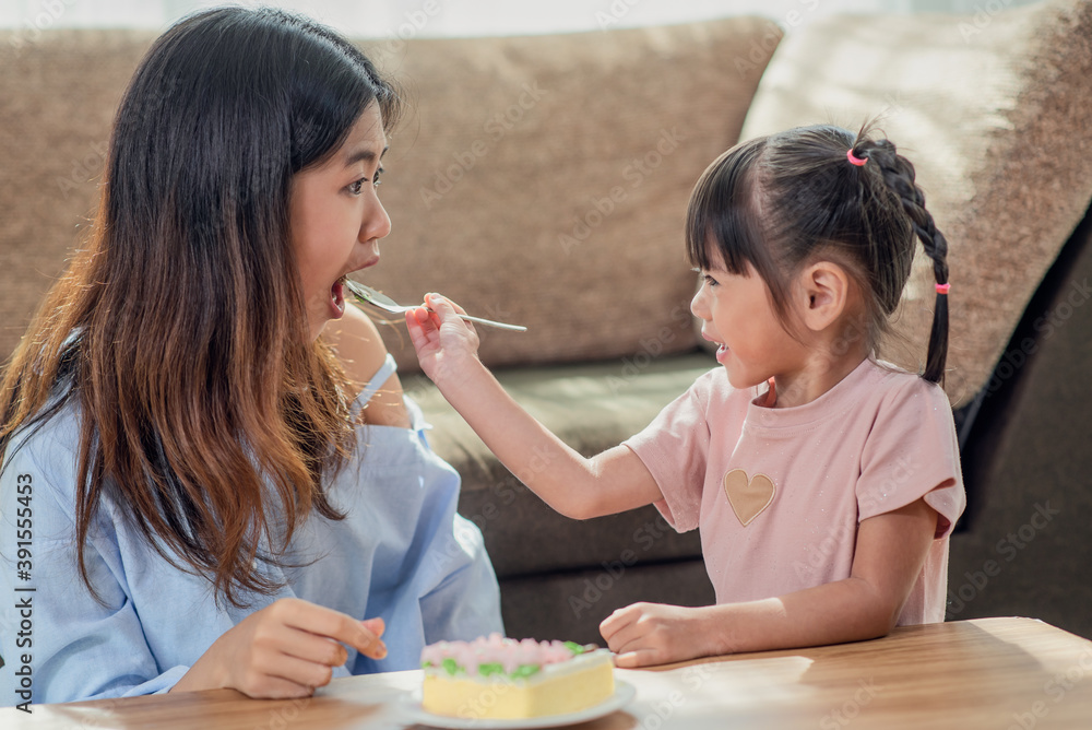 Asian younger sister feeding her older sister with spoon of tasty cake Asian younger sister feeding her older sister with spoon of tasty cake