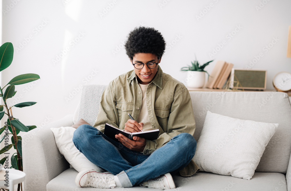 Focused African American student taking notes in copybook, working on school project at home