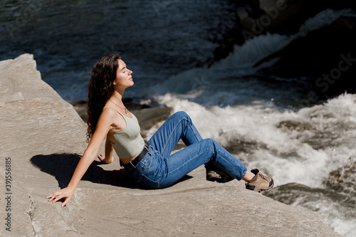 Traveler girl is sitting on the rock near waterfall and looking toward. Travelling in Karpathian mountains. Cascade waterfall. Beautiful landscape © Rabizo Anatolii