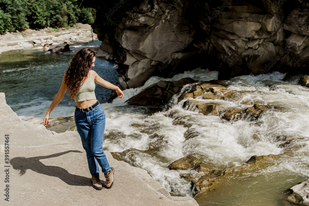 Girl is travelling in Karpathian mountains and feeling freedom. Waterfall in mountain river. Cascade waterfall and beautiful young woman